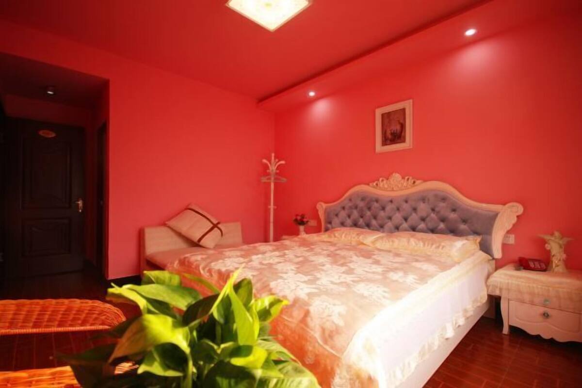 A bedroom with a large bed, a nightstand, a chair, and a potted plant.