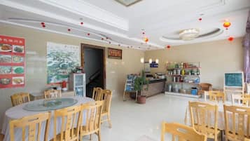 A restaurant with round tables and chairs, a counter with a menu, and a wall with food images.