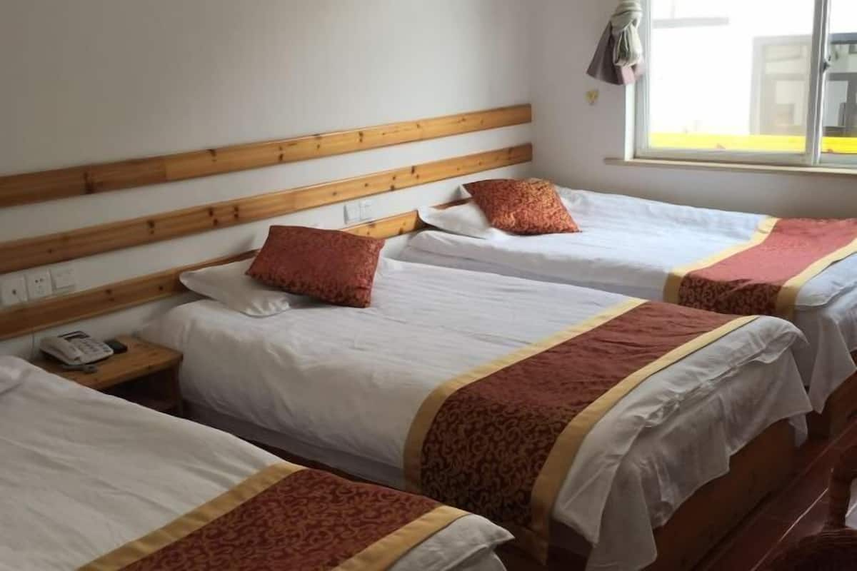 A hotel room with three single beds, wooden headboards, white bedding, and a window with a view.