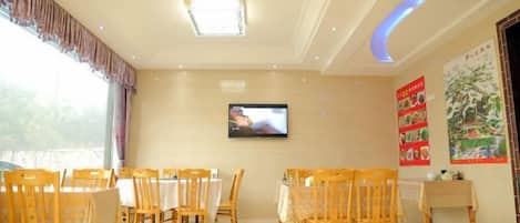 A dining area with tables and chairs, a television on the wall, and a poster.
