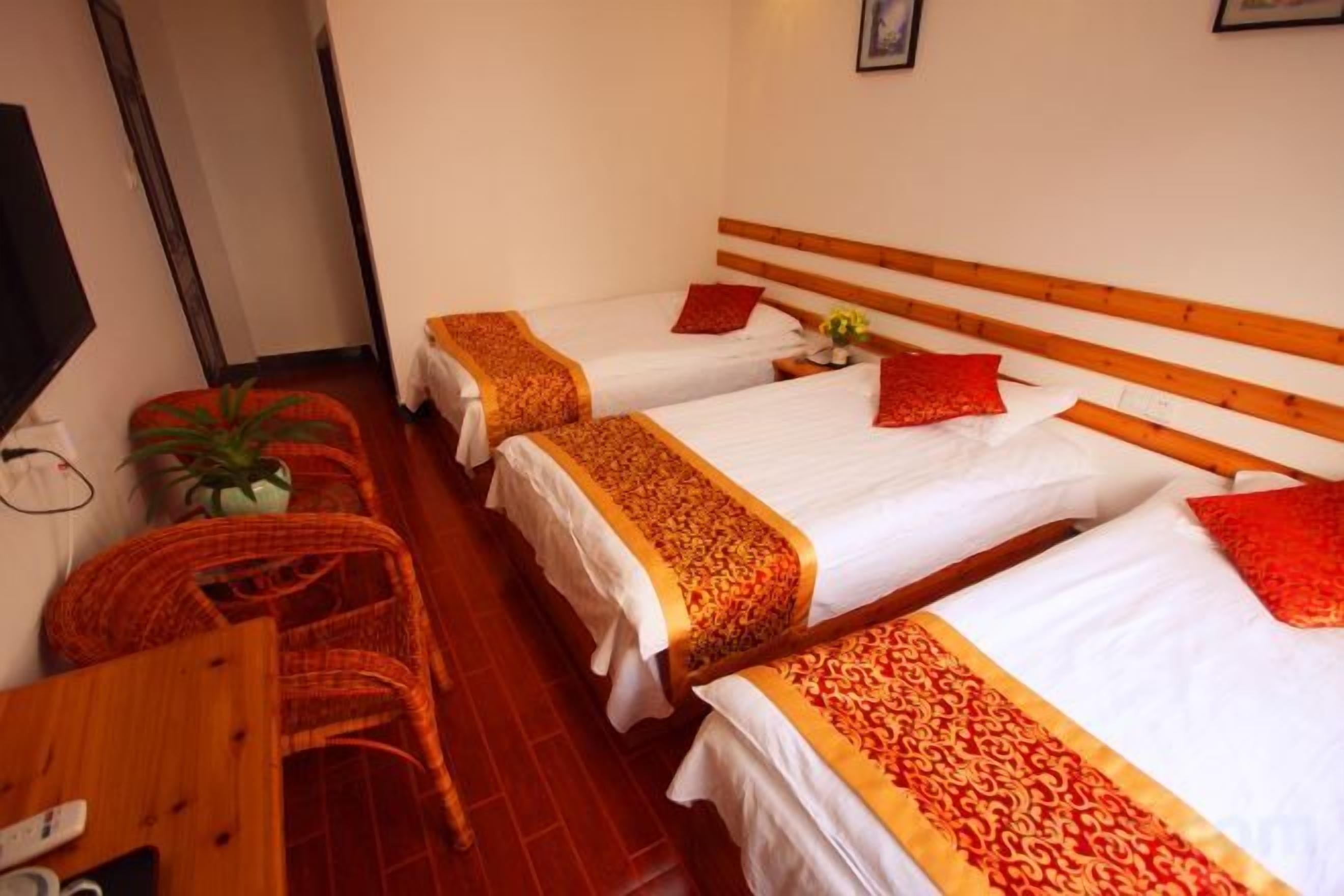A hotel room with three single beds, a wooden desk, a chair, and a potted plant.