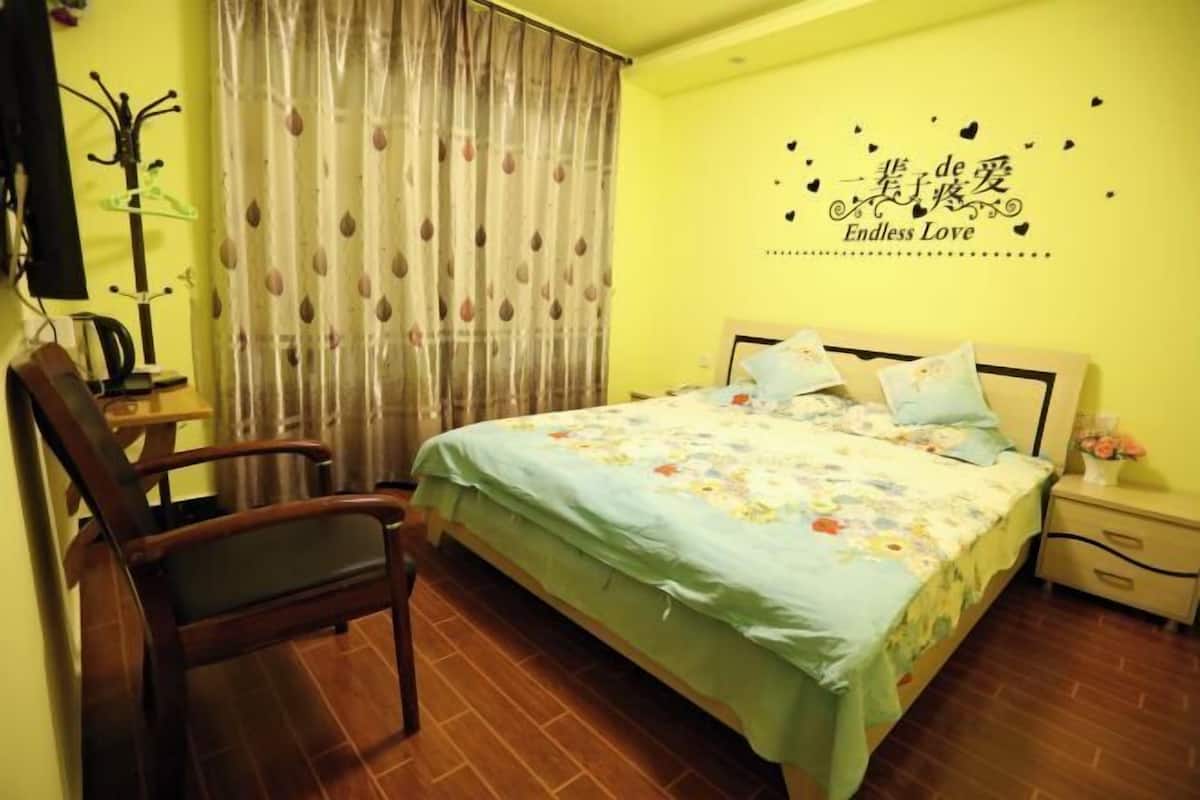 A bedroom with a bed, a chair, a nightstand, a wall decoration, and a curtain.