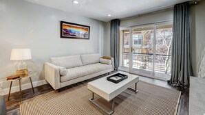Ein modernes Wohnzimmer mit einer Couch, einem Couchtisch, einer Lampe, einem Deckenventilator und einem großen Fenster mit Vorhängen.
