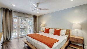Ein Hotelzimmer mit einem großen Bett, zwei Nachttischen mit Lampen, einem Deckenventilator und Blick ins Freie durch eine Schiebetür.