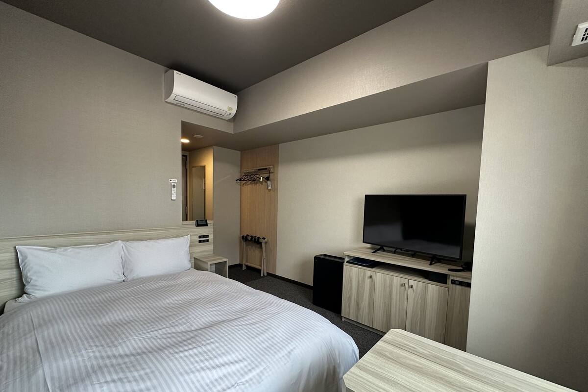 Ein Hotelzimmer mit einem großen Bett, einem Fernseher, einem Schreibtisch und einem Kleiderschrank.