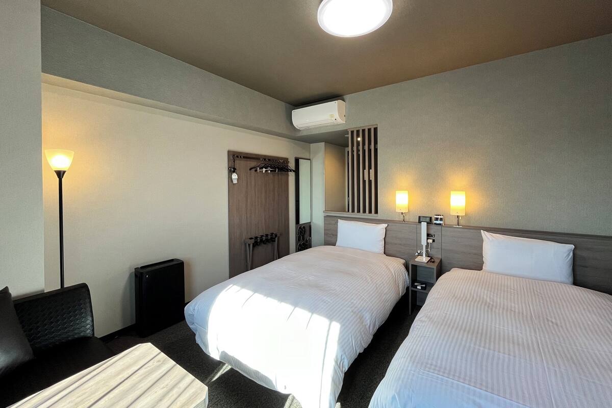 Ein Hotelzimmer mit zwei Betten, einem Schreibtisch, einem Stuhl, einer Lampe und einem Spiegel.