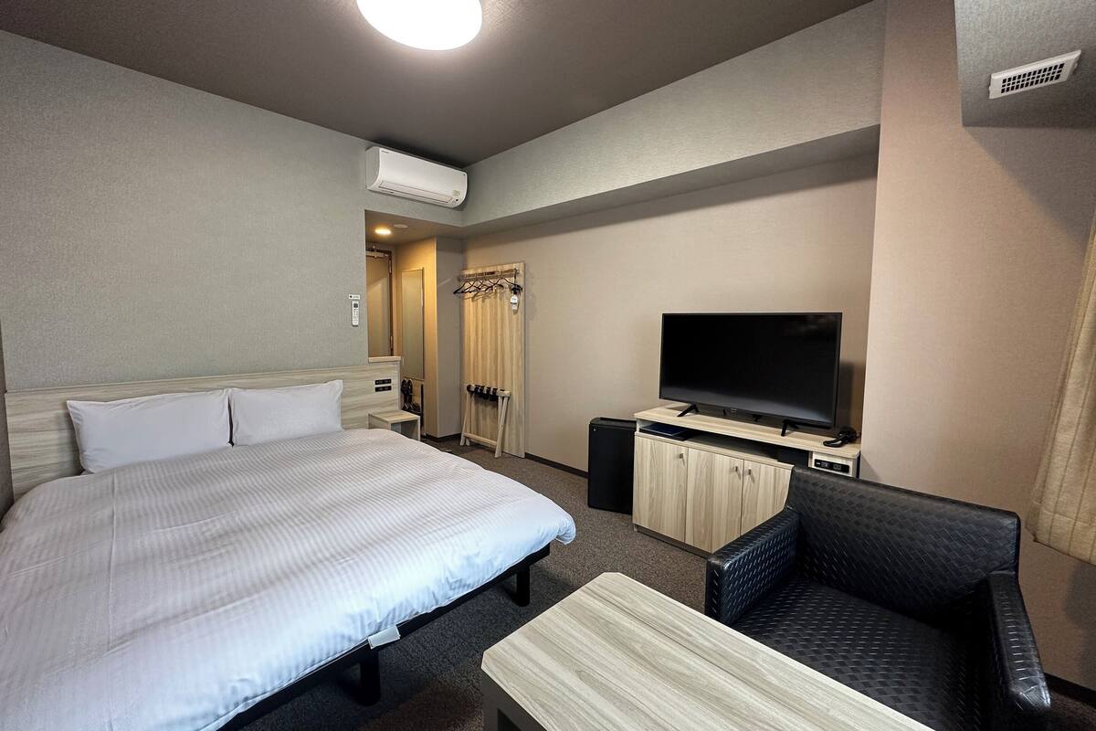 Ein Hotelzimmer mit einem großen Bett, einem Flachbildfernseher, einem kleinen Tisch, einem Sessel und einem Kleiderschrank.