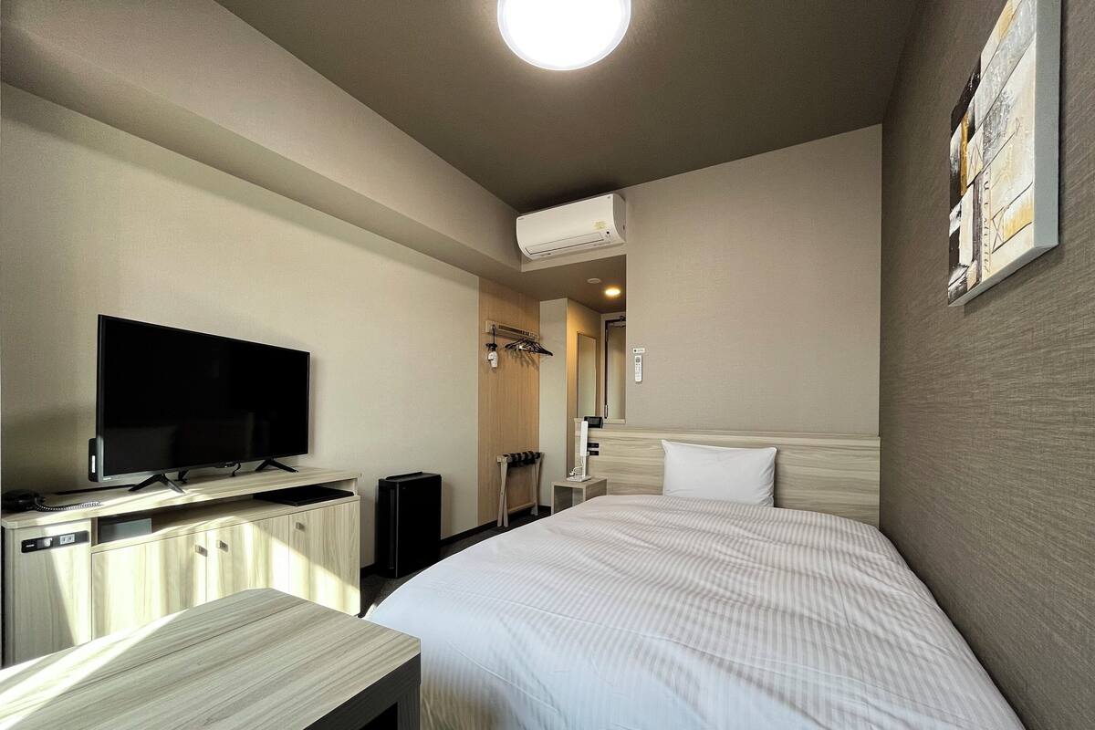 Ein Hotelzimmer mit Bett, Fernseher, Schreibtisch und Kleiderschrank.
