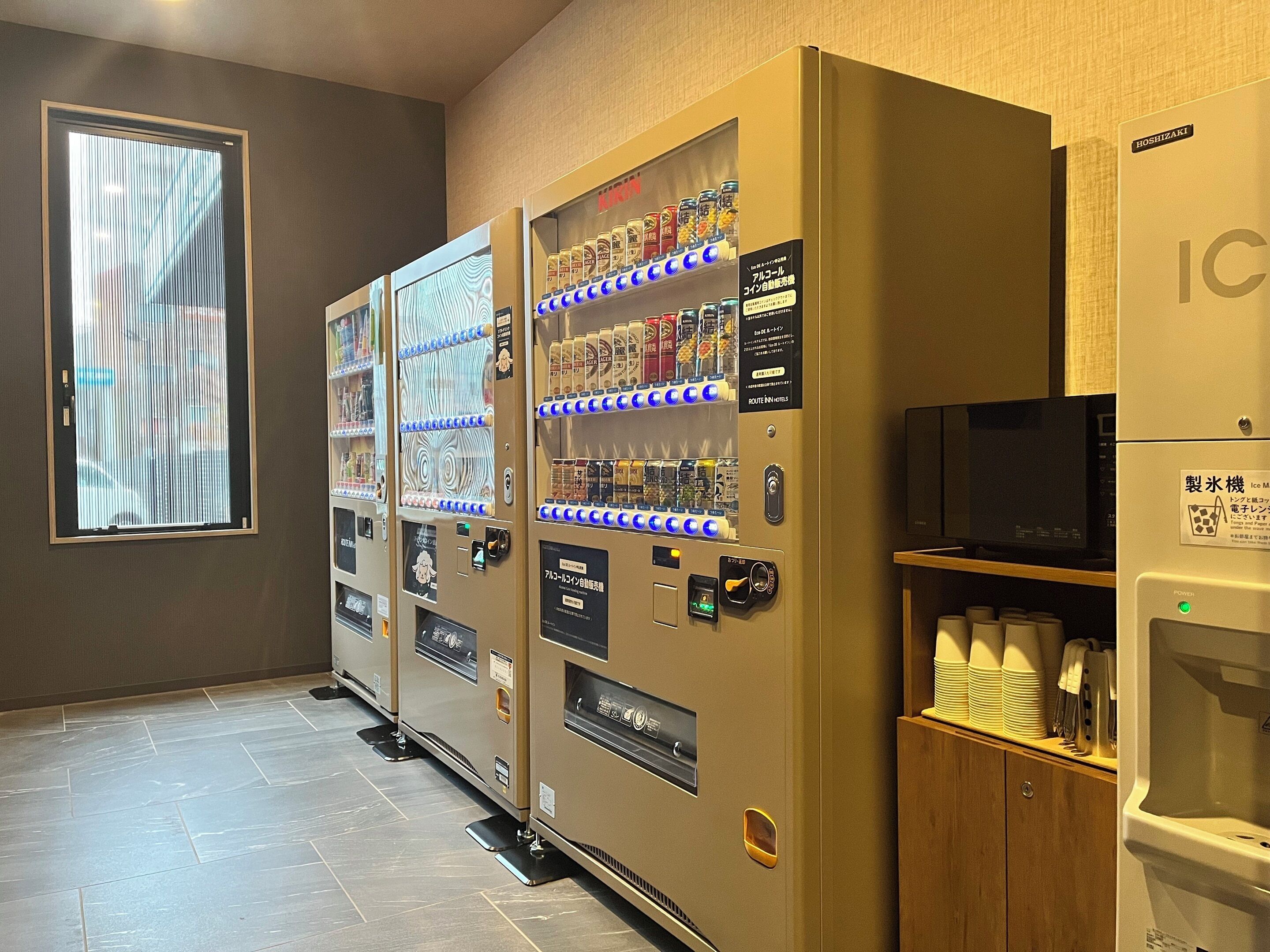 Una fila de máquinas expendedoras con bebidas y aperitivos, un microondas y un dispensador de agua en una habitación de hotel.