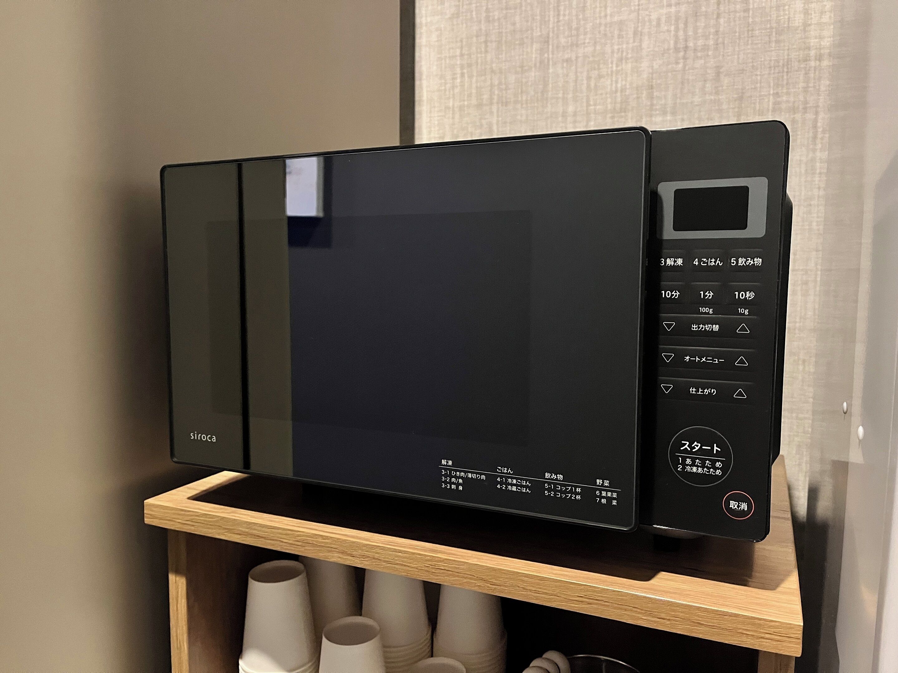 Un horno microondas negro con pantalla digital y panel de control, sobre un estante de madera.