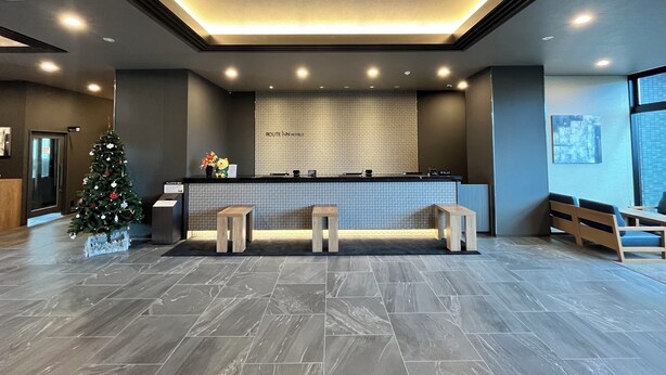 A modern hotel reception area with a tiled floor, a reception desk, and a Christmas tree. - Hotel Route Inn Miyakonojo (Miyakonojo)