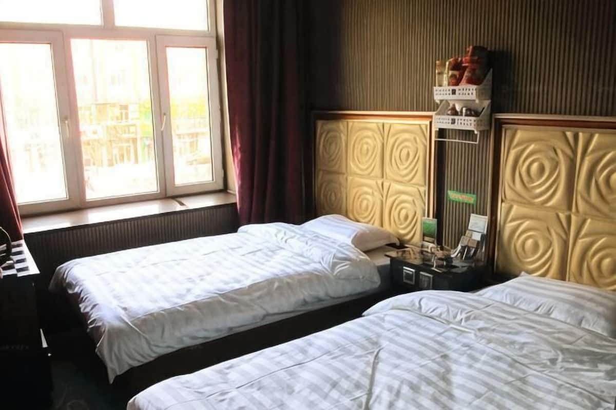 Een hotelkamer met twee bedden, een bureau, een raam met gordijnen en een wandplank met spullen.