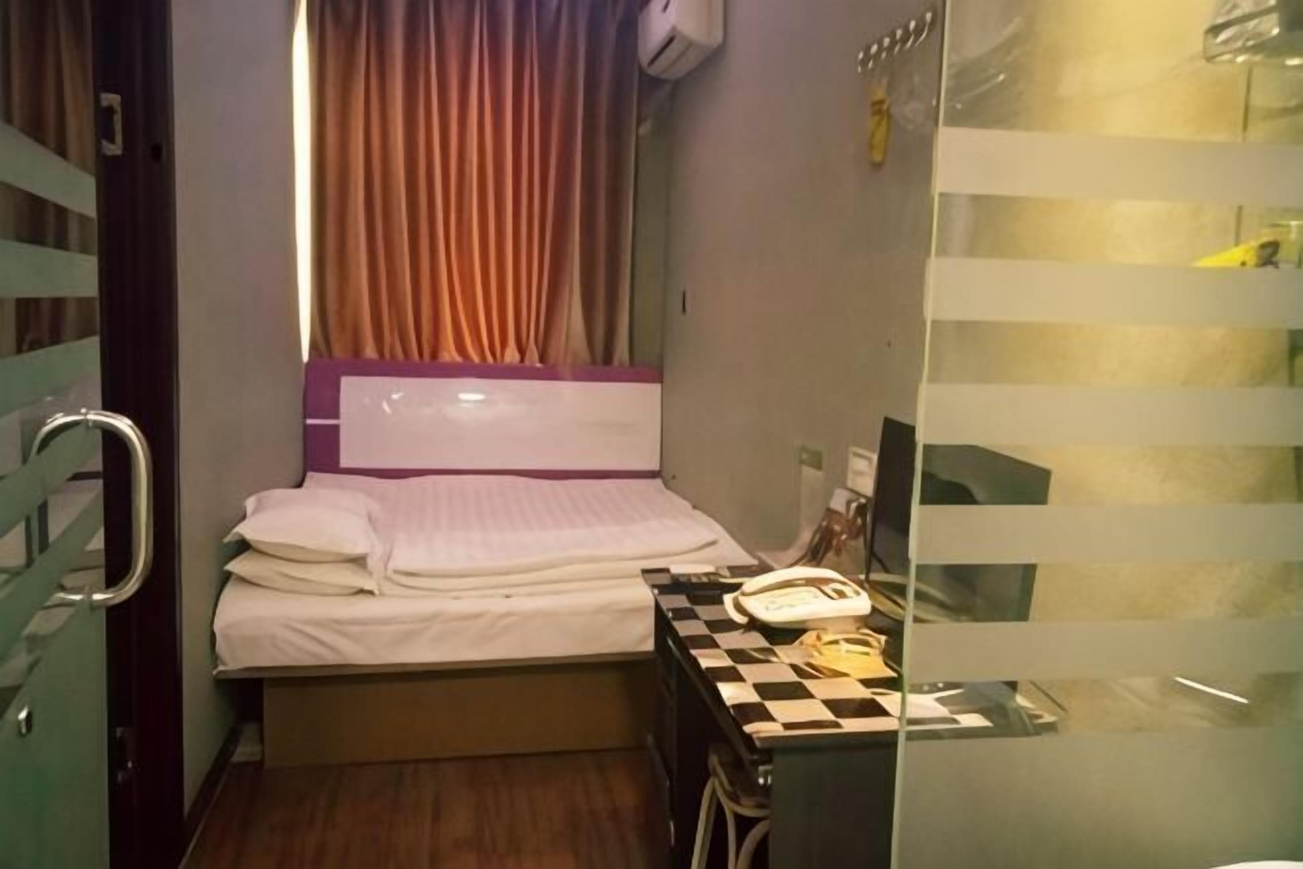 Una habitación de hotel pequeña con una cama, un escritorio con teléfono y una ventana con cortinas.