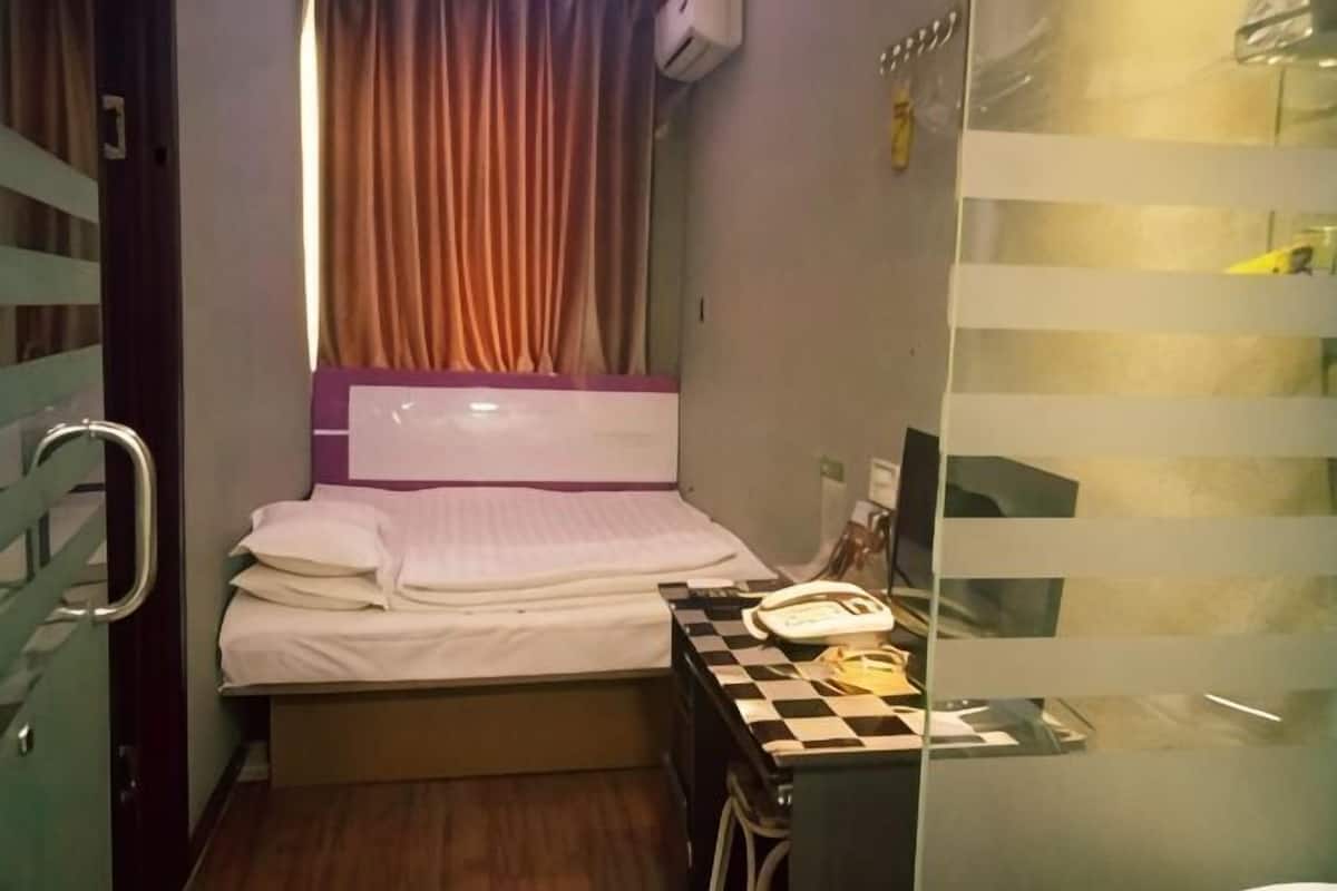 Een compacte hotelkamer met een bed, een bureau met telefoon en een raam met gordijnen.