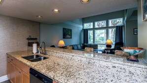 A kitchen with granite countertops, a dishwasher, a sink, a dining area with a table and chairs, and a window with curtains. - 493 Egrets Pointe-Beautiful Townhome on Lagoon; Pool/Amenity Access Included (Edisto Beach)