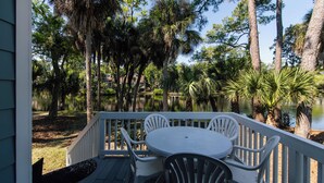 A deck with a table and chairs overlooking a lake, surrounded by tall trees and a wooden fence. - 493 Egrets Pointe-Beautiful Townhome on Lagoon; Pool/Amenity Access Included (Edisto Beach)