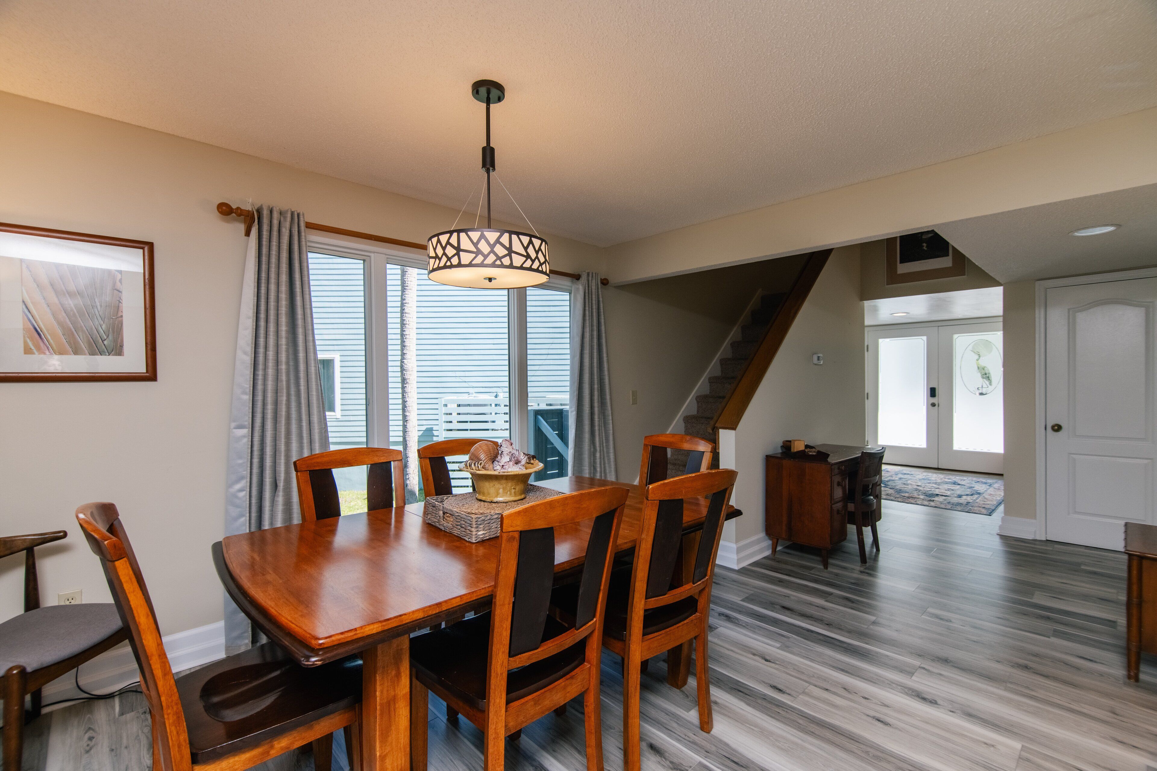 A dining area with a wooden table and chairs, a hanging light fixture, and a view of a staircase and door.