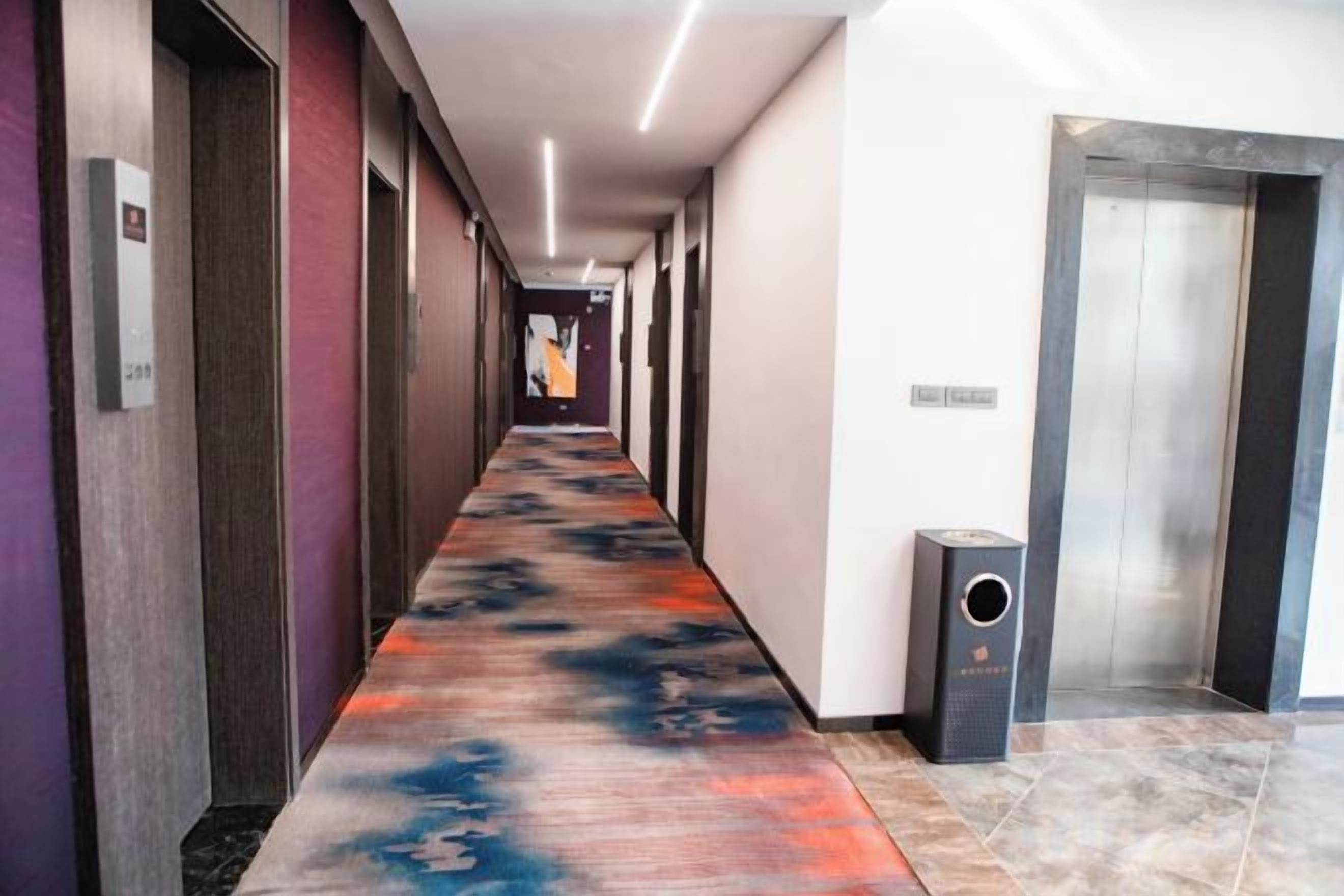 A hotel corridor with a patterned carpet, doors, and an elevator.