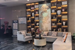 A modern lobby with a sectional sofa, a round coffee table, and a wall-mounted bookshelf. - XiaoNanJing Fashion Hotel (Shangli)