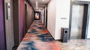 En lang gang med et mønstret tæppe, døre på den ene side og en elevator på den anden.