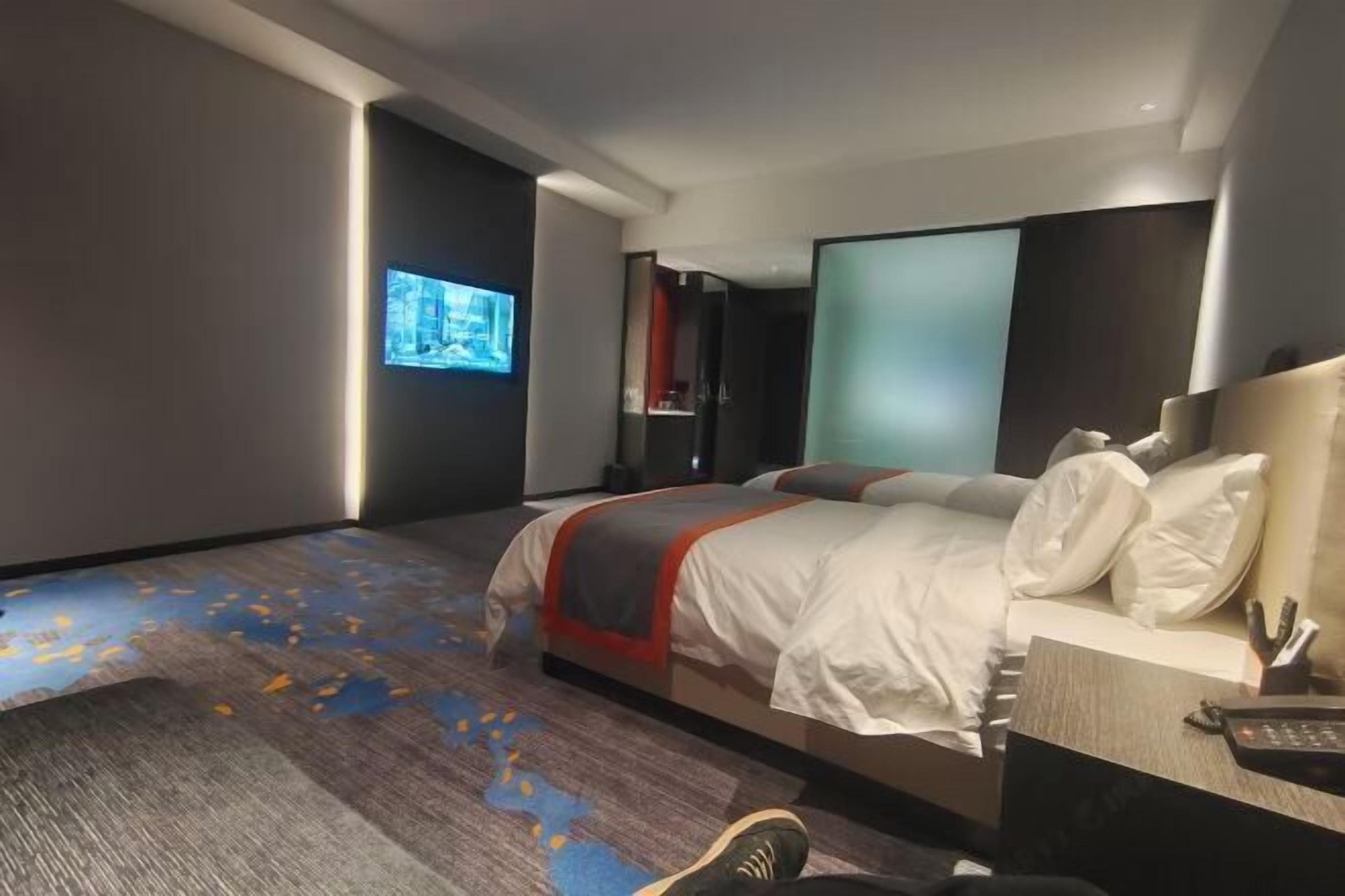 A modern hotel room with a bed, a TV, a desk with a phone, and a carpet with a geometric pattern.