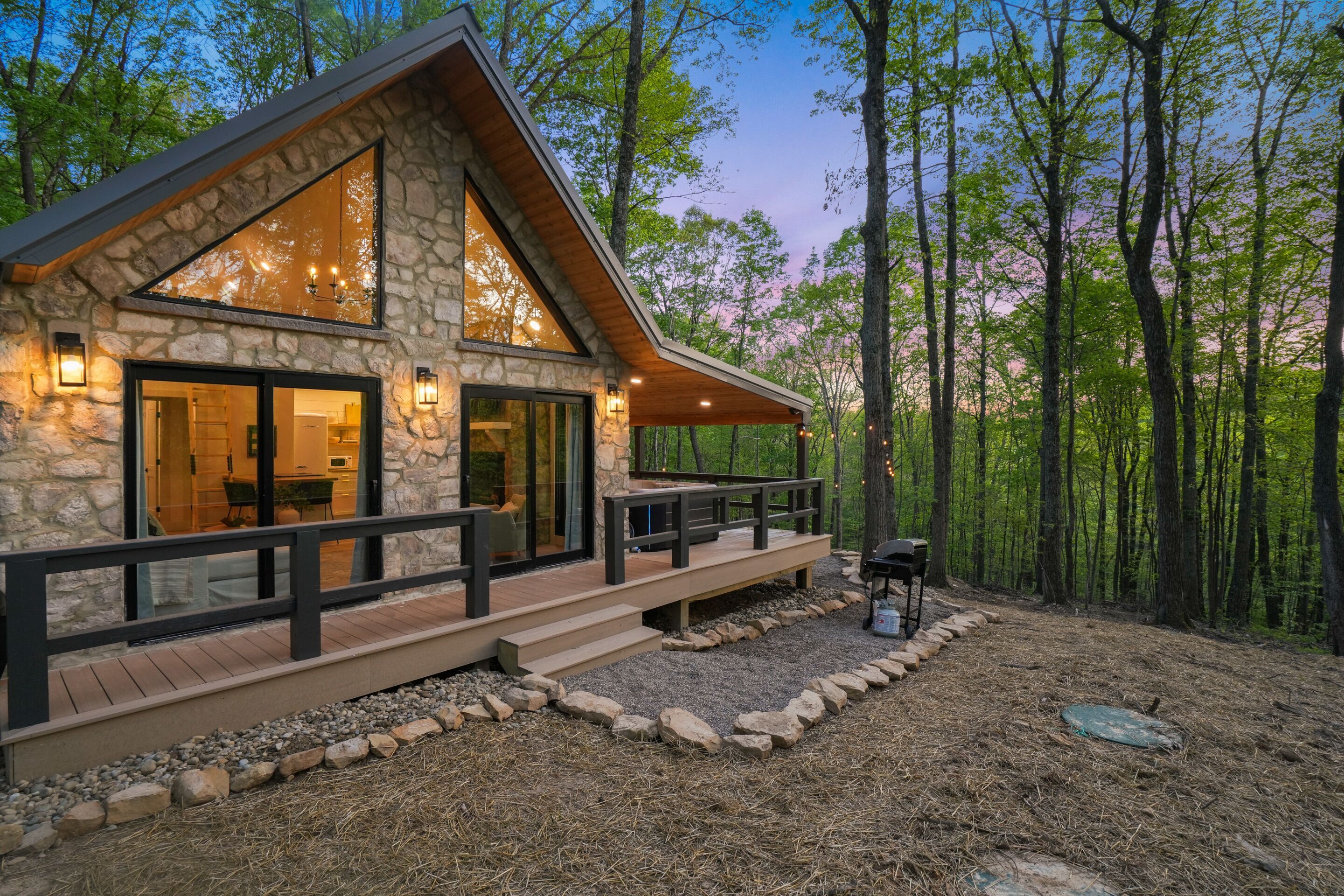 A stone cabin with a large deck, a barbecue area, and a view of the surrounding forest.