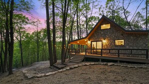 A stone cabin with a wooden deck, surrounded by trees. - Uckor's Cottage | Hocking Hills, 5 Acres, Hot Tub (Rockbridge)