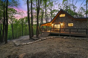 A stone cabin with a wooden deck, surrounded by trees. - Uckor's Cottage | Hocking Hills, 5 Acres, Hot Tub (Rockbridge)