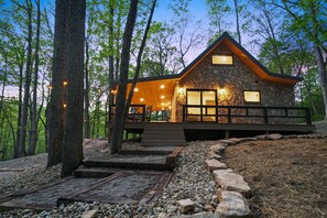 A stone cabin with a wooden deck and large windows, surrounded by trees. - Uckor's Cottage | Hocking Hills, 5 Acres, Hot Tub (Rockbridge)