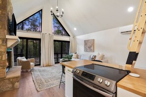 A modern kitchen with a large window, a built-in stove, and a cozy seating area. - Uckor's Cottage | Hocking Hills, 5 Acres, Hot Tub (Rockbridge)