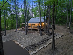 A cabin with a stone exterior, wooden deck, and a fire pit area. - Uckor's Cottage | Hocking Hills, 5 Acres, Hot Tub (Rockbridge)