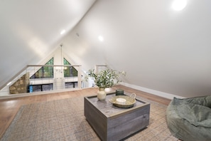 A modern loft bedroom with a sloped ceiling, a wooden floor, a large window, and a view of a balcony. - Uckor's Cottage | Hocking Hills, 5 Acres, Hot Tub (Rockbridge)