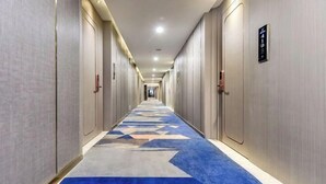 A long, narrow hotel corridor with a patterned carpet and doors on both sides.