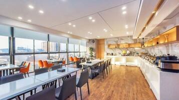 Un comedor moderno de hotel con mesas largas, sillas y una cocina al fondo.