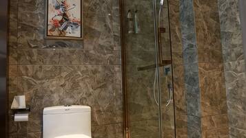 Un baño con inodoro, cabina de ducha de vidrio y pared de mármol.