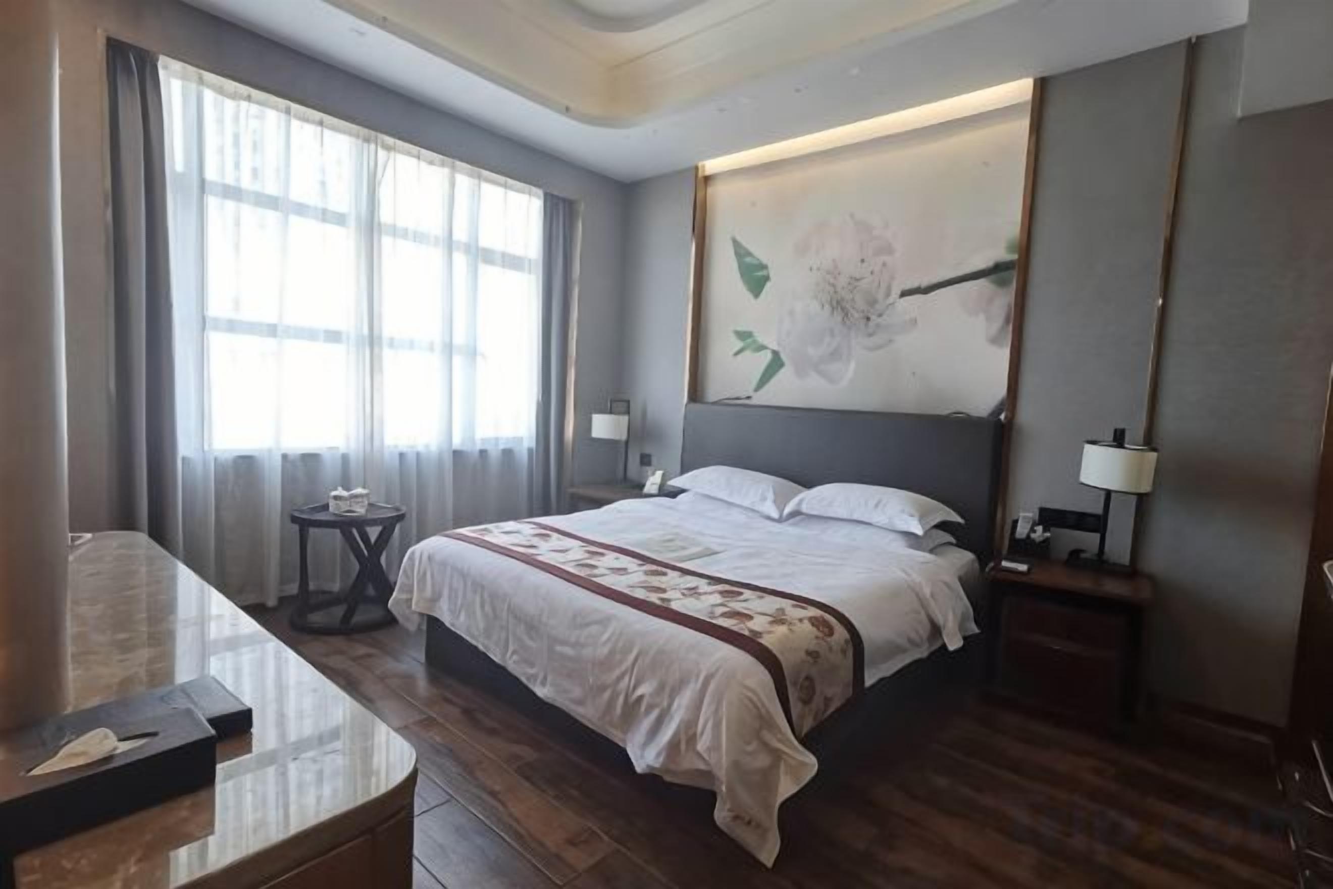A hotel room with a large bed, bedside tables, a desk, and a window with curtains.