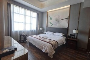 Una habitación de hotel con una cama grande, mesitas de noche, un escritorio y una ventana con cortinas.
