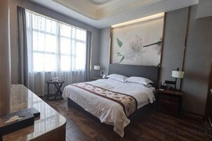 A hotel room with a large bed, bedside tables, a desk, and a window with curtains.