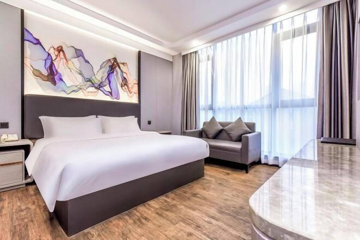 Una habitación de hotel moderna con una cama grande, un sofá, una mesita de mármol y un cuadro abstracto de grandes dimensiones en la pared.