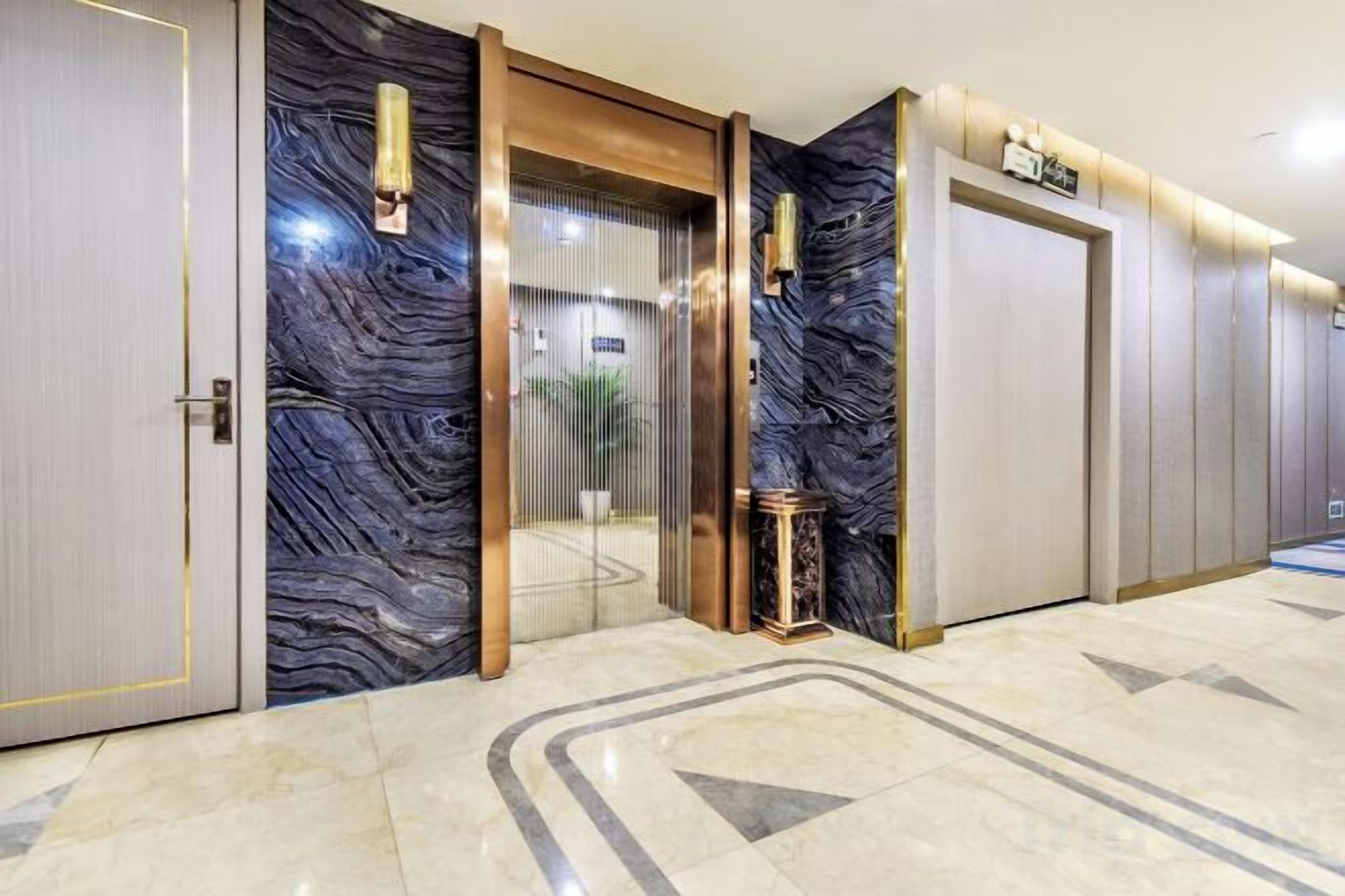 Un vestíbulo de hotel con piso de mármol, una recepción y un ascensor de vidrio.