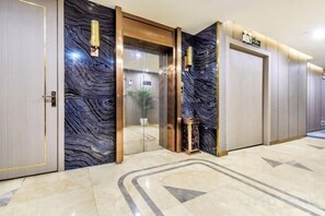 Un vestíbulo de hotel con piso de mármol, una recepción y un ascensor de vidrio.