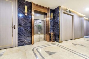 A hotel lobby with a marble floor, a reception desk, and a glass elevator.