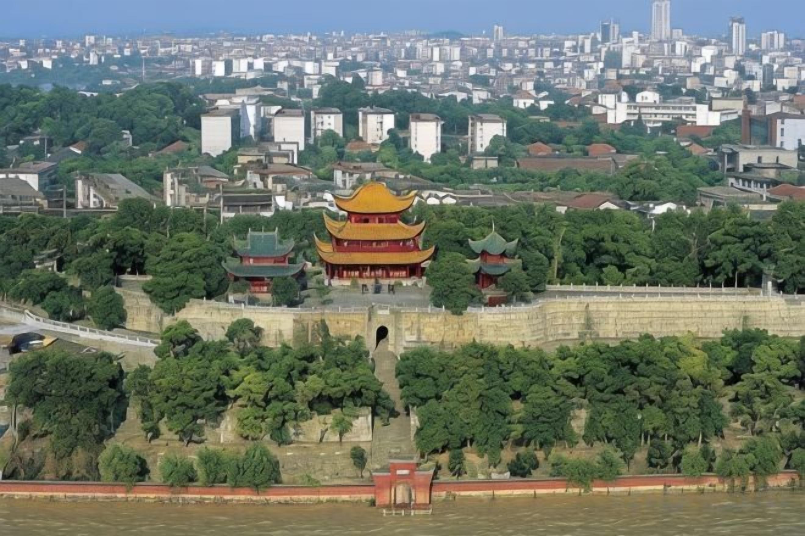 A traditional Chinese building with a multi-tiered roof, surrounded by greenery and a cityscape in the background.