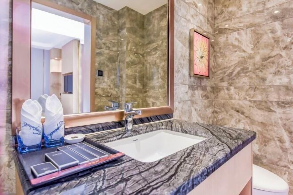 A bathroom with a marble sink, a large mirror, and a framed artwork on the wall.