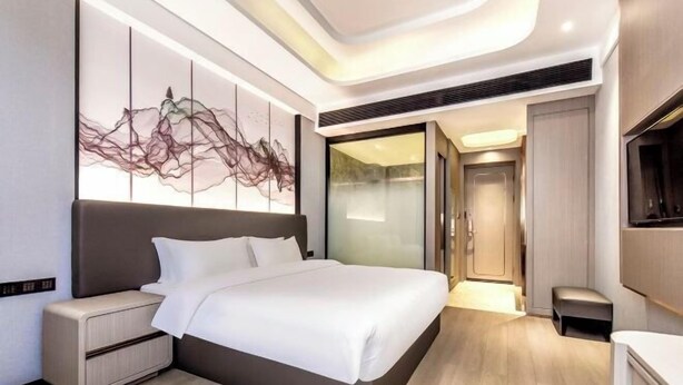 A modern hotel room with a large bed, a bedside table, a wall-mounted artwork, and a sliding door leading to a bathroom.