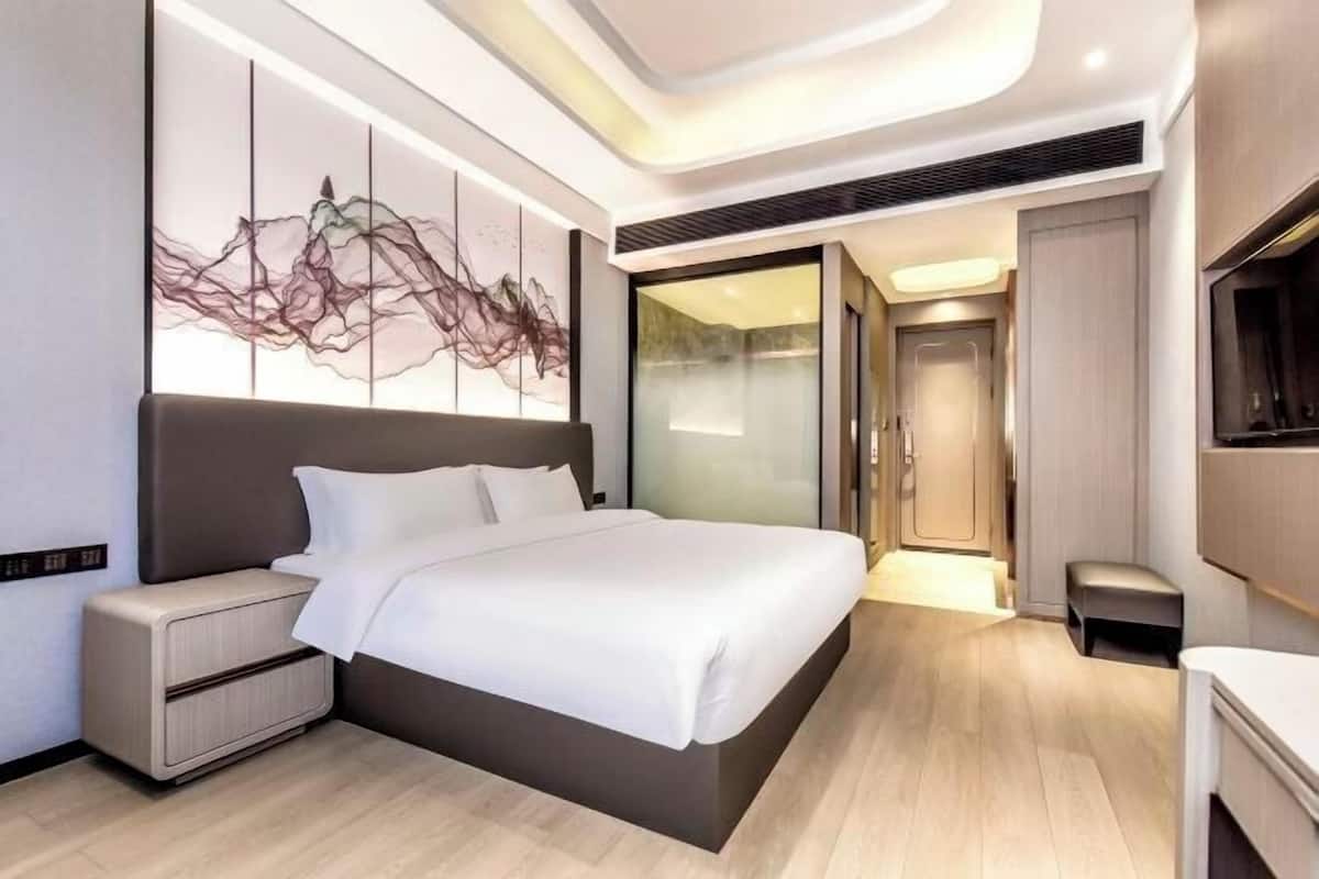 Una habitación de hotel moderna con una cama grande, una mesita de noche, una obra de arte en la pared y una puerta corredera que da al baño.