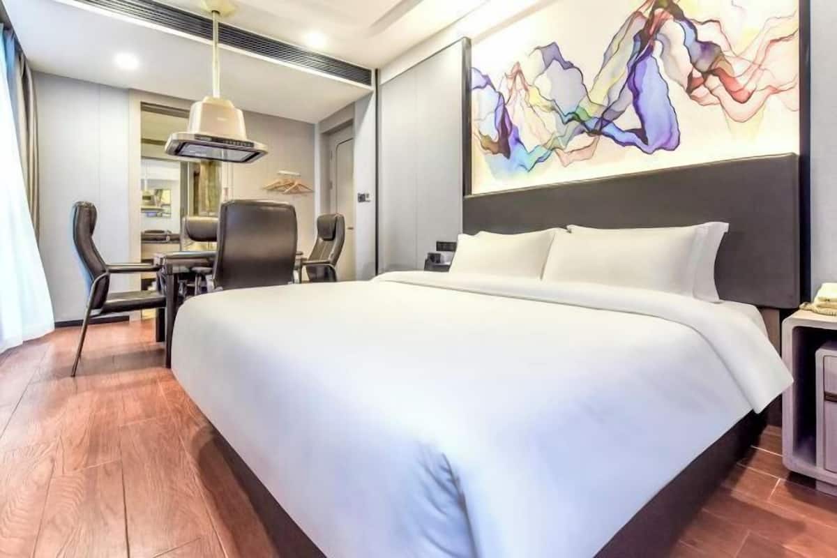Una habitación de hotel moderna con una cama grande, un área de comedor y un cuadro abstracto y colorido en la pared.