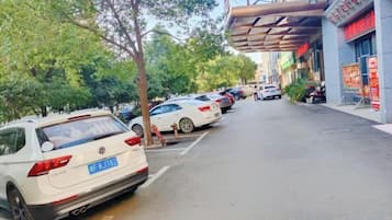 A street lined with parked cars and trees, with a building featuring a sign with Chinese characters.