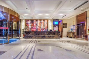 Un hall de hotel con una recepción, un cuadro abstracto de gran tamaño y una entrada de cristal.