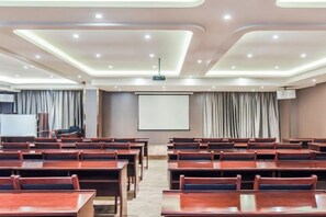 Une salle de conférence avec des rangées de tables et de chaises, un écran de projection et un écran de présentation.